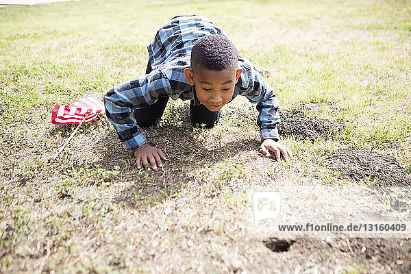 Boy crawling  peering into hole in ground