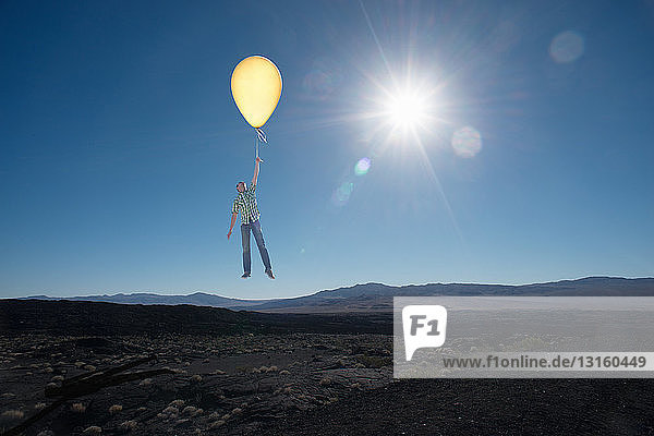 Mittlerer erwachsener Mann schwebt mit Ballon in der Wüste