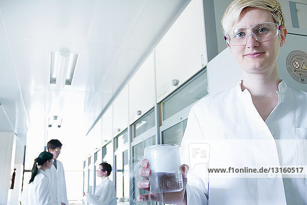 Chemiestudent hält Becher mit Flüssigkeit im Labor  Porträt