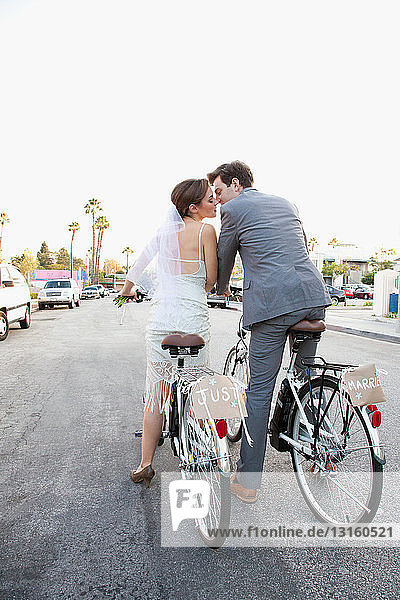 Young newlywed couple kissing on bicycles in street