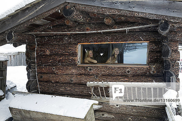 Two young women at log cabin sauna window