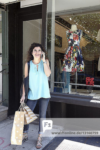 Ältere Frau verlässt eine Modeboutique mit Einkaufstaschen und Smartphone