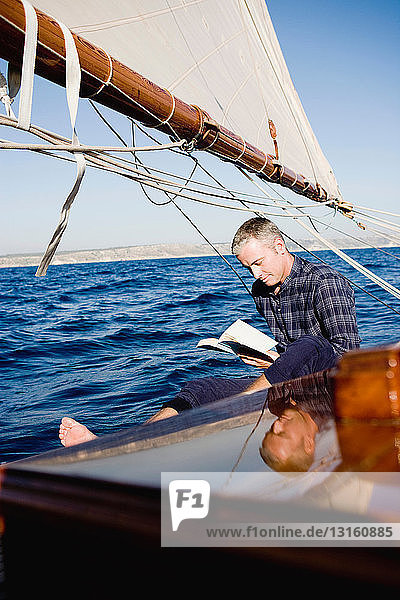 Mann lesend auf einem Segelboot sitzend