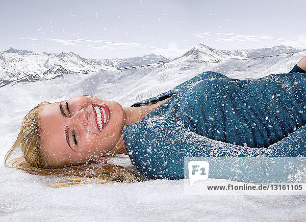 Junge Frau lacht im Schnee liegend