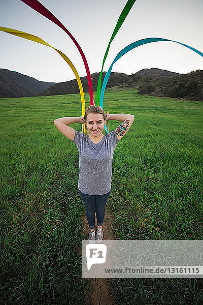 Porträt einer jungen Frau  die auf einem Feld steht und mit Tanzbändern ein Muster bildet