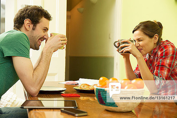 Junges Paar mit Kaffeetassen in der Hand  Frau blinzelt über den Rand