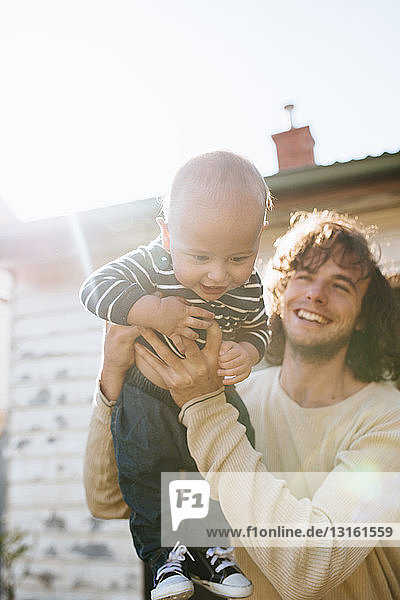 Father holding up son in arms beside house