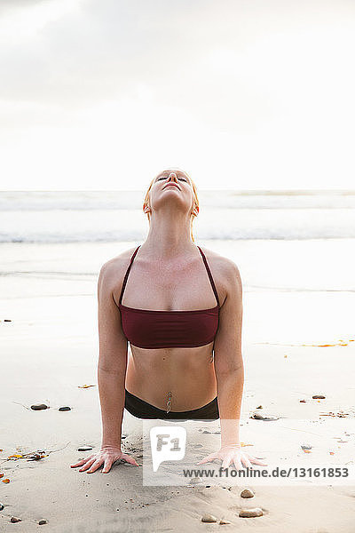 Mittlere erwachsene Frau  die eine Planken-Yoga-Pose am Strand praktiziert