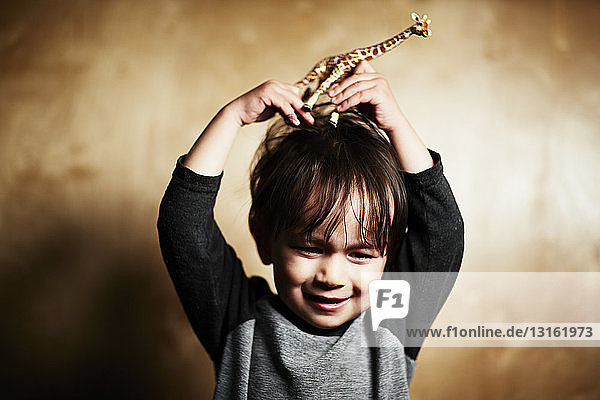 Porträt eines süßen männlichen Kleinkindes  das eine Spielzeuggiraffe auf dem Kopf hält