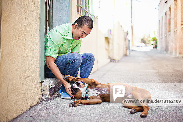 Mittelgroßer erwachsener Mann spielt mit seinem Boxerhund auf der Türschwelle