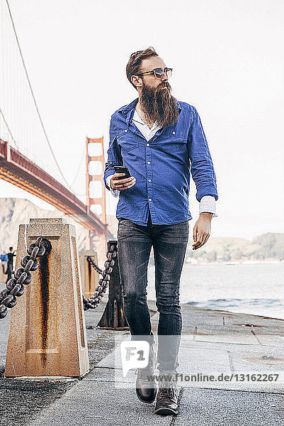 Man with beard checking smartphone at Golden Gate Bridge  San Francisco  California  USA