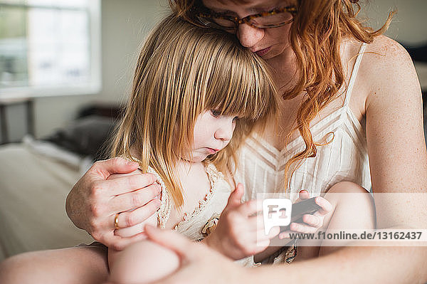 Mother hugging daughter  using smartphone