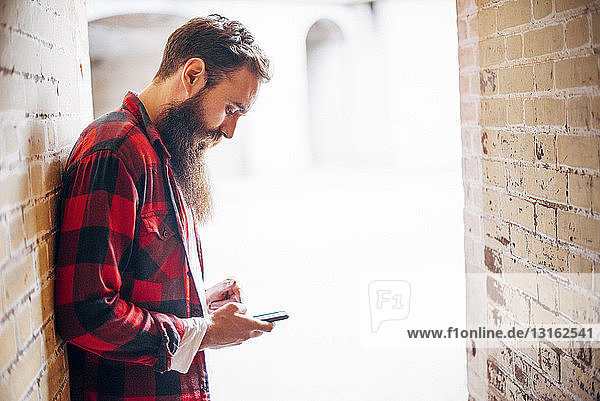 Seitenansicht eines Mannes mit Bart  der ein Smartphone hält
