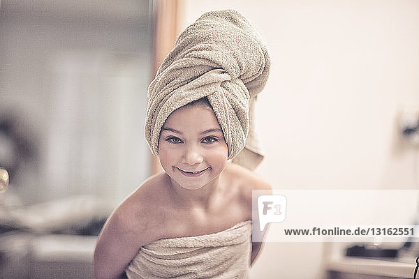 In Handtuch gewickeltes Mädchen mit Handtuch auf dem Kopf schaut lächelnd in die Kamera