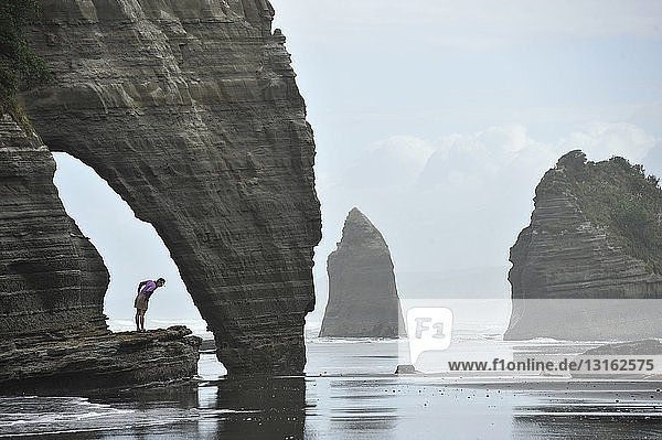 Junge Frau schaut von einer Felsformation am Strand hinunter  Nordinsel  Neuseeland