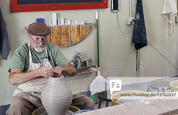 Töpfer mit flacher Kappe sitzt an einer Tonvase  die eine Töpferscheibe formt