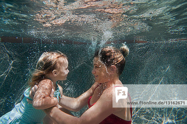 Unterwasseraufnahme einer Mutter  die ihre Tochter hält und ihr beim Schwimmenlernen hilft