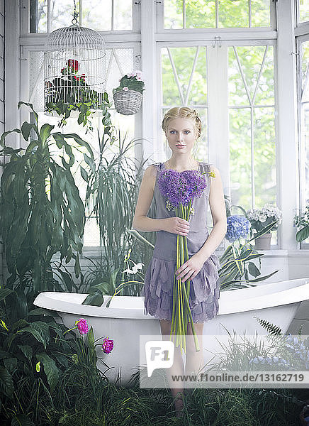 Junge Frau mit Blumenstrauss in der Hand  steht im Badezimmer voller Pflanzen