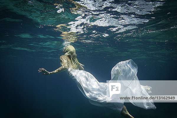 Young woman wearing wedding dress  swimming underwater  rear view
