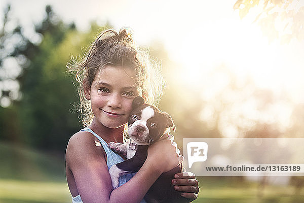 Mädchen hält Boston-Terrier-Welpen Wange an Wange und schaut lächelnd in die Kamera