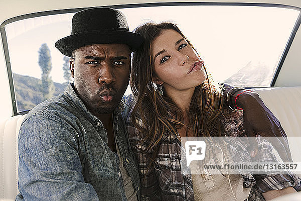Portrait of couple pulling faces in back seat of car