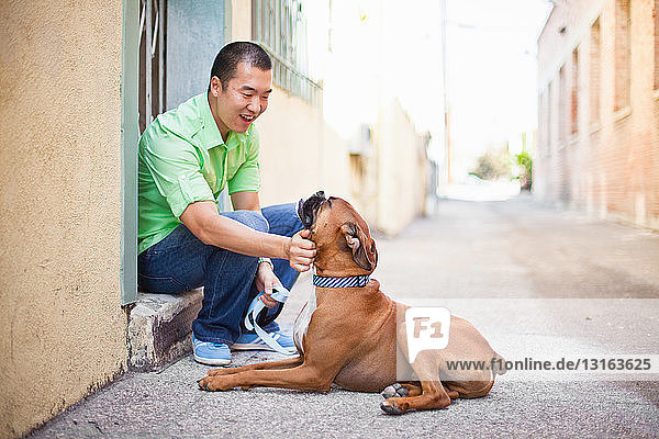 Mittelgroßer erwachsener Mann streichelt seinen Boxerhund auf der Türschwelle