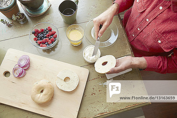 Overhead view of man spreading soft cheese on bagel