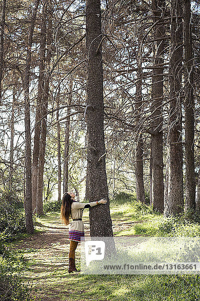 Junge Frau umarmt Baumstamm im Wald