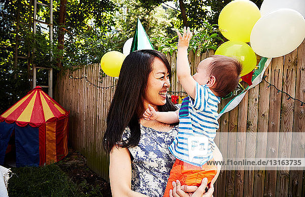 Mutter trägt Parteihut mit Babyjunge auf Geburtstagsfeier