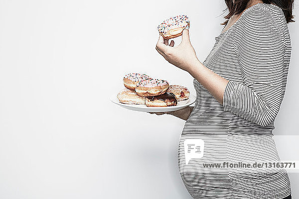Schwangere Frau hält Teller mit Donuts