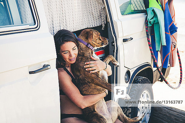 Frau sitzt im Wohnmobil und umarmt Haushund