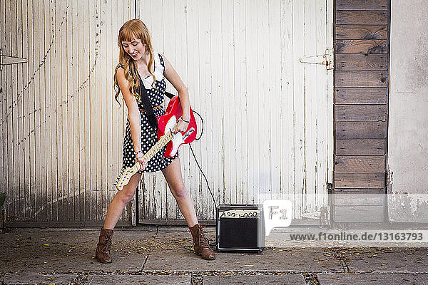 Young woman playing electric guitar outside garage