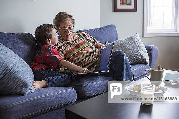 Ältere Frau erklärt ihrem Enkel das Buch  während sie auf dem Sofa liest