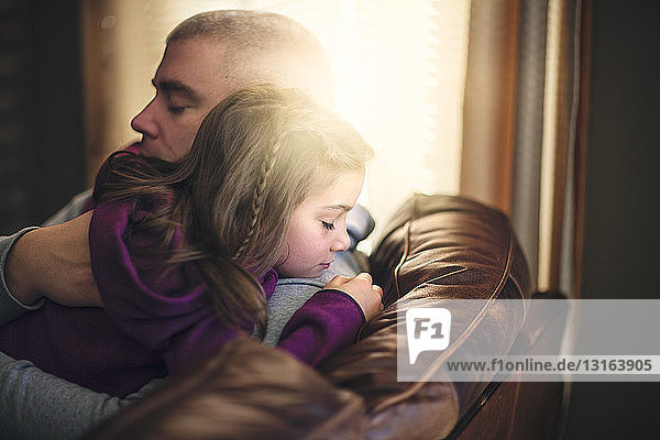 Reifer Mann entspannt sich auf Sofa und umarmt Tochter