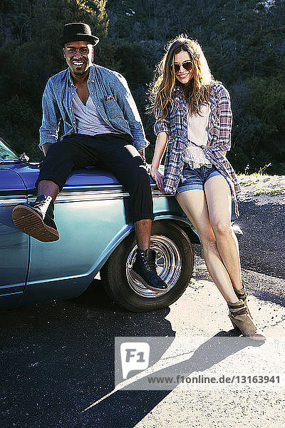 Portrait of couple sitting and leaning against vintage car