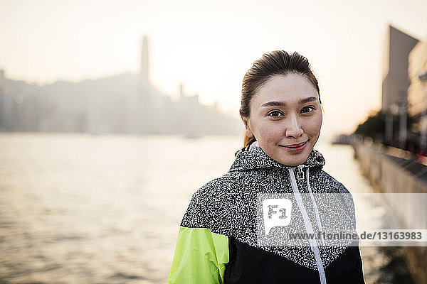 Porträt einer jungen Frau im Trainingsanzug vor dem Wasser lächelnd