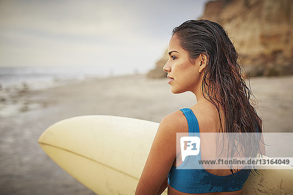 Rückansicht einer jungen Frau  die ein Surfbrett am Strand trägt  San Diego  Kalifornien  USA