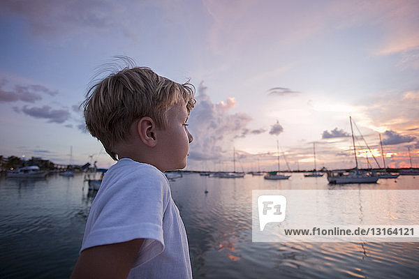 Junge auf Segelboot schaut bei Sonnenuntergang aufs Meer hinaus