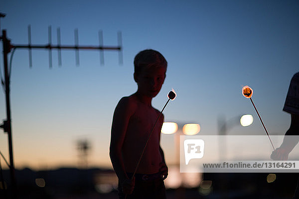 Silhouette von Teenager-Jungen  die schwelende Marshmallows auf Stöcken halten