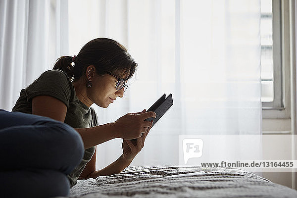 Frau benutzt digitales Tablett am Bett