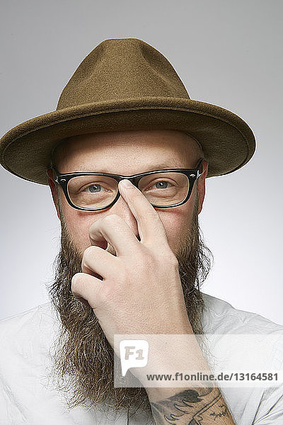 Studioporträt eines mittleren erwachsenen Mannes in Trilby mit Gesicht  das die Hand versteckt