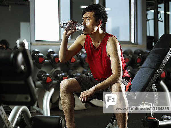Man sitting on weight bench drinking bottle of water