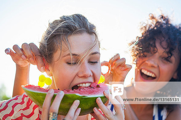 Junge Frau isst Wassermelone  während ihr Freund an den Ohren zieht