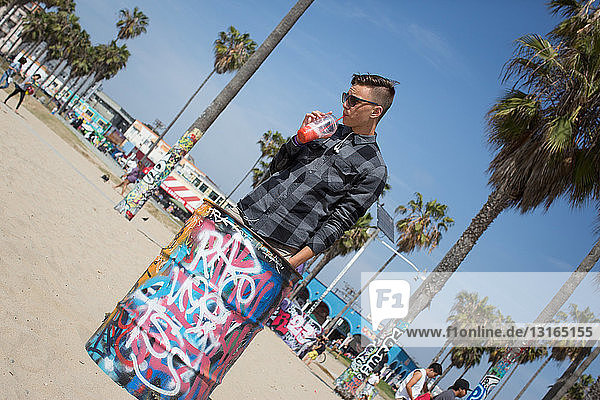 Schräger Blick auf Teenager  der Smoothie neben einem mit Graffiti bedeckten Mülleimer trinkt  Los Angeles  Kalifornien  USA