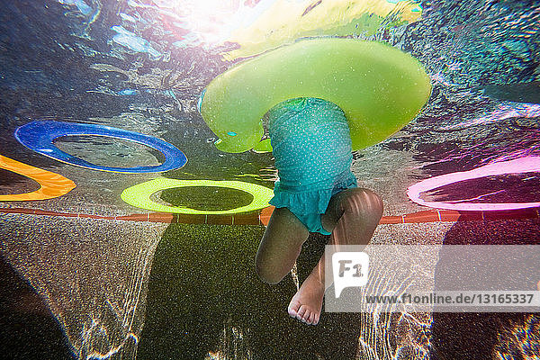 Unterwasseraufnahme eines Mädchens  das im Schwimmbad mit einem Gummiring gegen die Beine tritt und schwimmen lernt