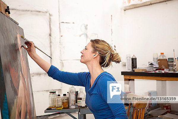 Mittlere erwachsene Frau malt auf Leinwand im Künstleratelier