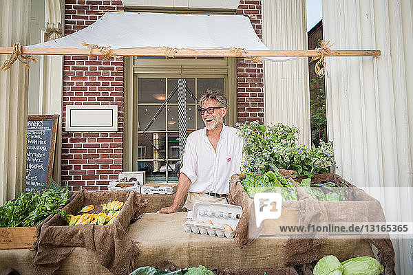 Farmer selling organic eggs and vegetables on stall outside store