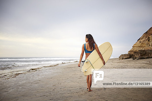Rückansicht einer jungen Frau  die mit einem Surfbrett am Strand spazieren geht  San Diego  Kalifornien  USA