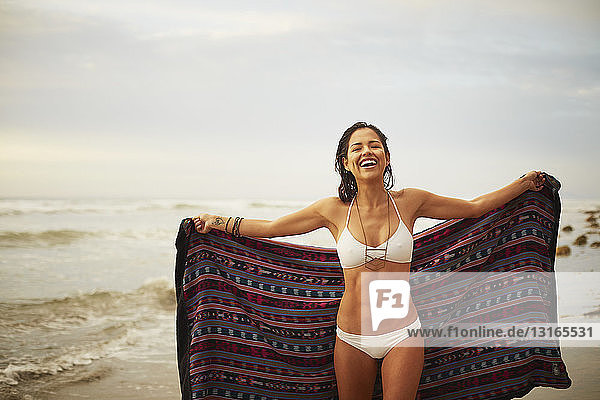 Portrait of young woman holding up blanket on beach  San Diego  California  USA