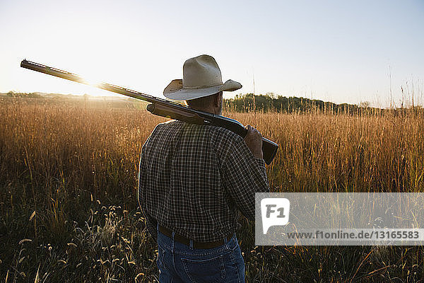 Älterer männlicher Landwirt mit Schrotflinte auf der Schulter auf einem abgelegenen Feld in der Abenddämmerung  Plattsburg  Missouri  USA